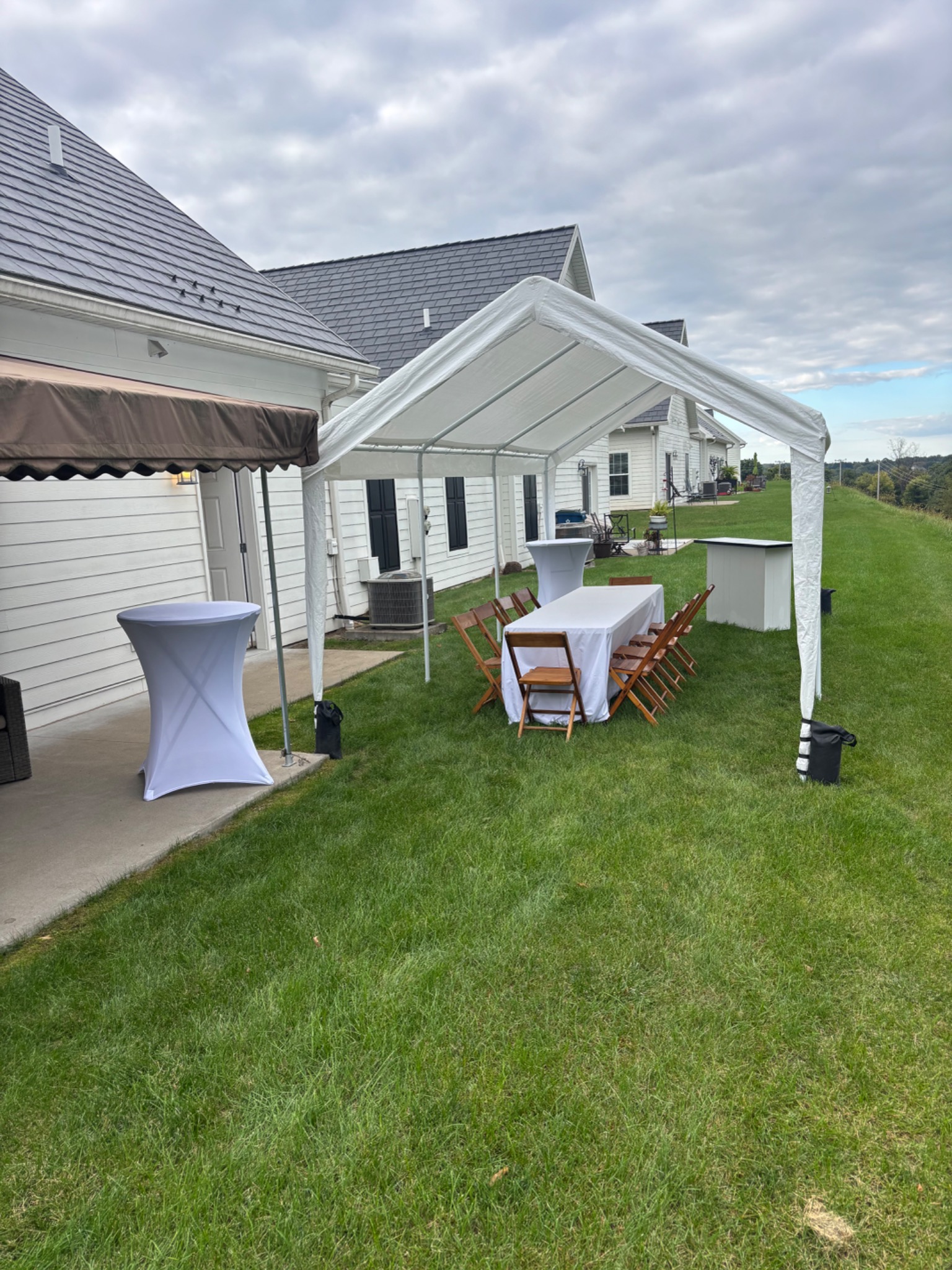 White backyard tent on a lawn with a linen-covered table, wooden chairs, cocktail tables and a mobile bar
