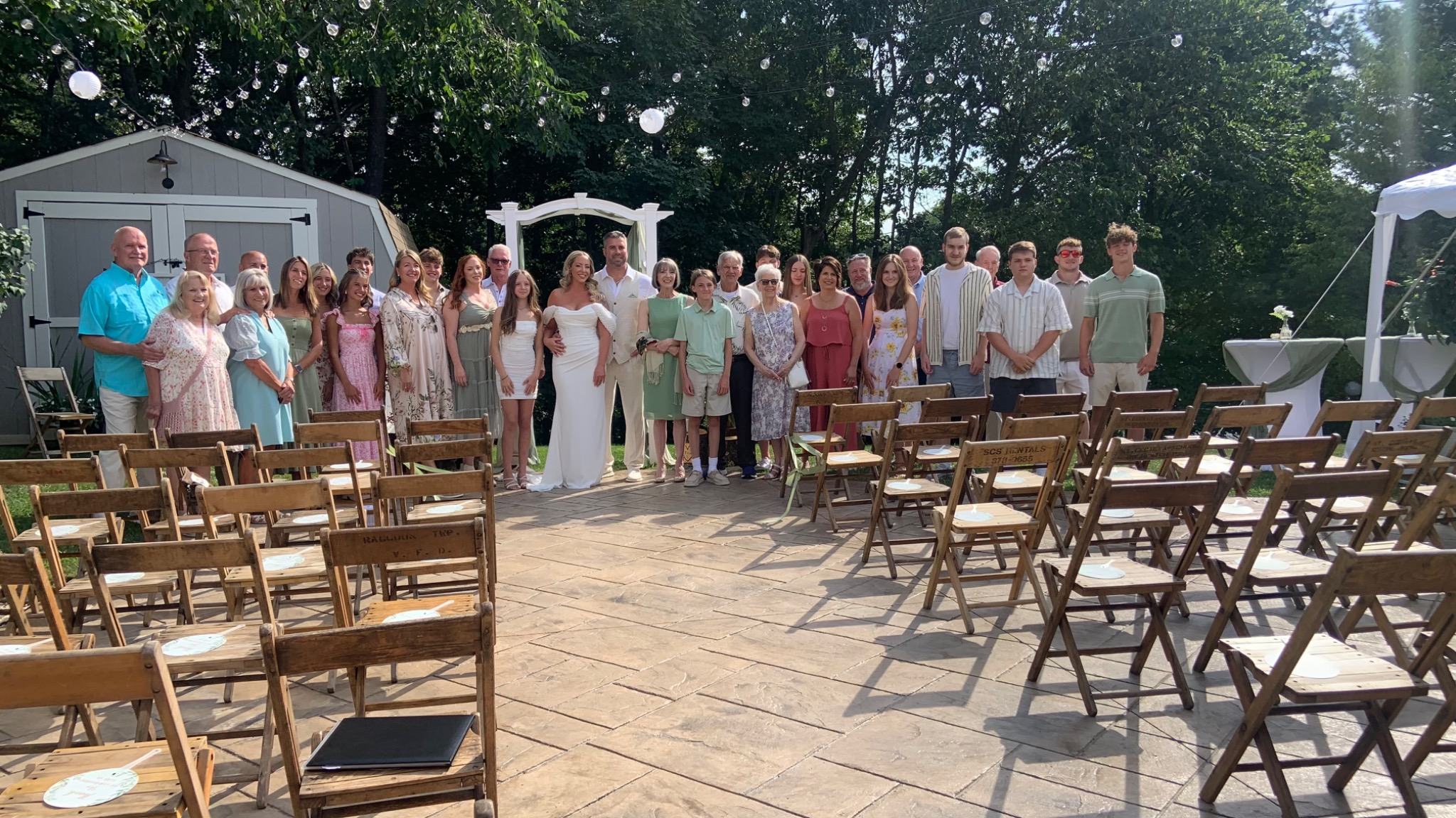 Backyard wedding guests gathered among wooden ceremony chairs